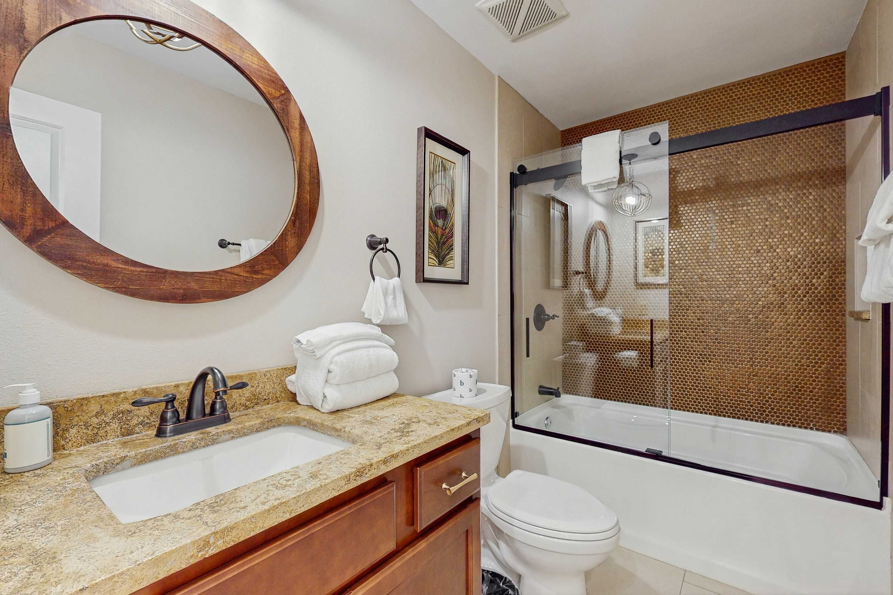 A bathroom with a sink, mirror, toilet, and glass-enclosed shower.