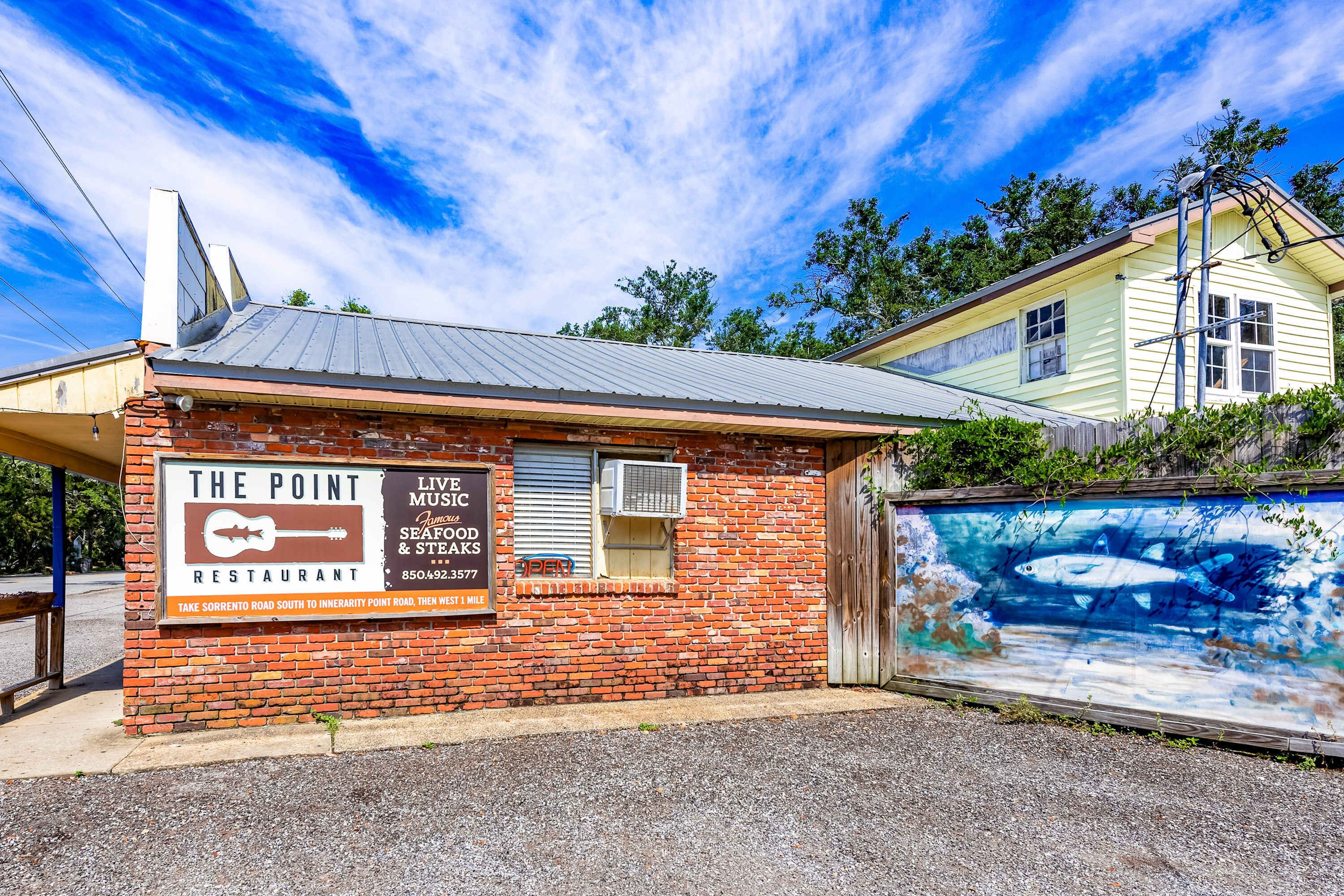 A brick building with a sign for 'The Point Restaurant' offering live music, seafood, and steaks.