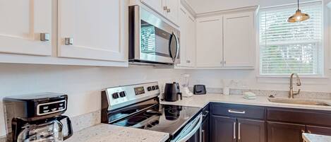 Une cuisine moderne avec des meubles blancs, une cuisinière en acier inoxydable, une machine à café et une fenêtre équipée de stores.