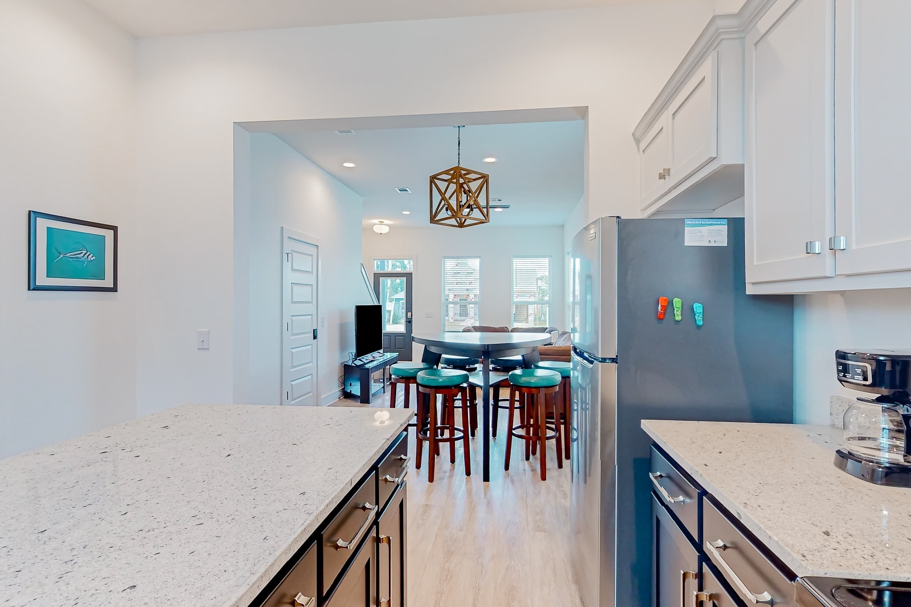 A modern kitchen with a central island, bar stools, and a refrigerator.