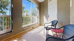 Ein Balkon mit weißer Brüstung, einem roten Tisch und zwei schwarzen Stühlen.