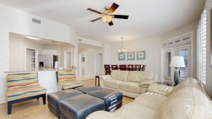 Ein geräumiges Wohnzimmer mit einem beigen Sofa, gestreiften Sesseln und einem Deckenventilator.