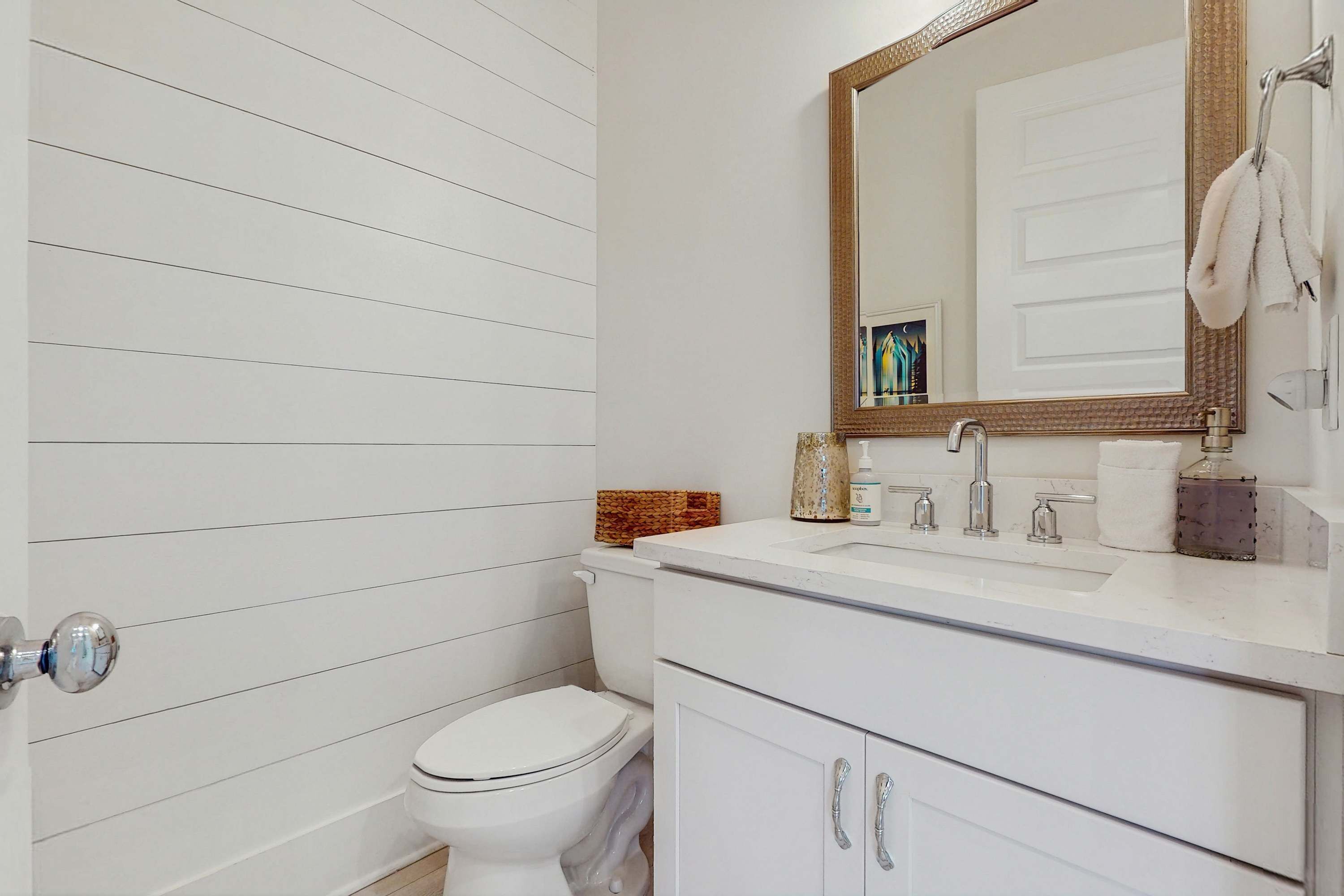 A bathroom with a white tiled wall, a white toilet, a white sink with a mirror above it, and a towel hanging on a towel rack.