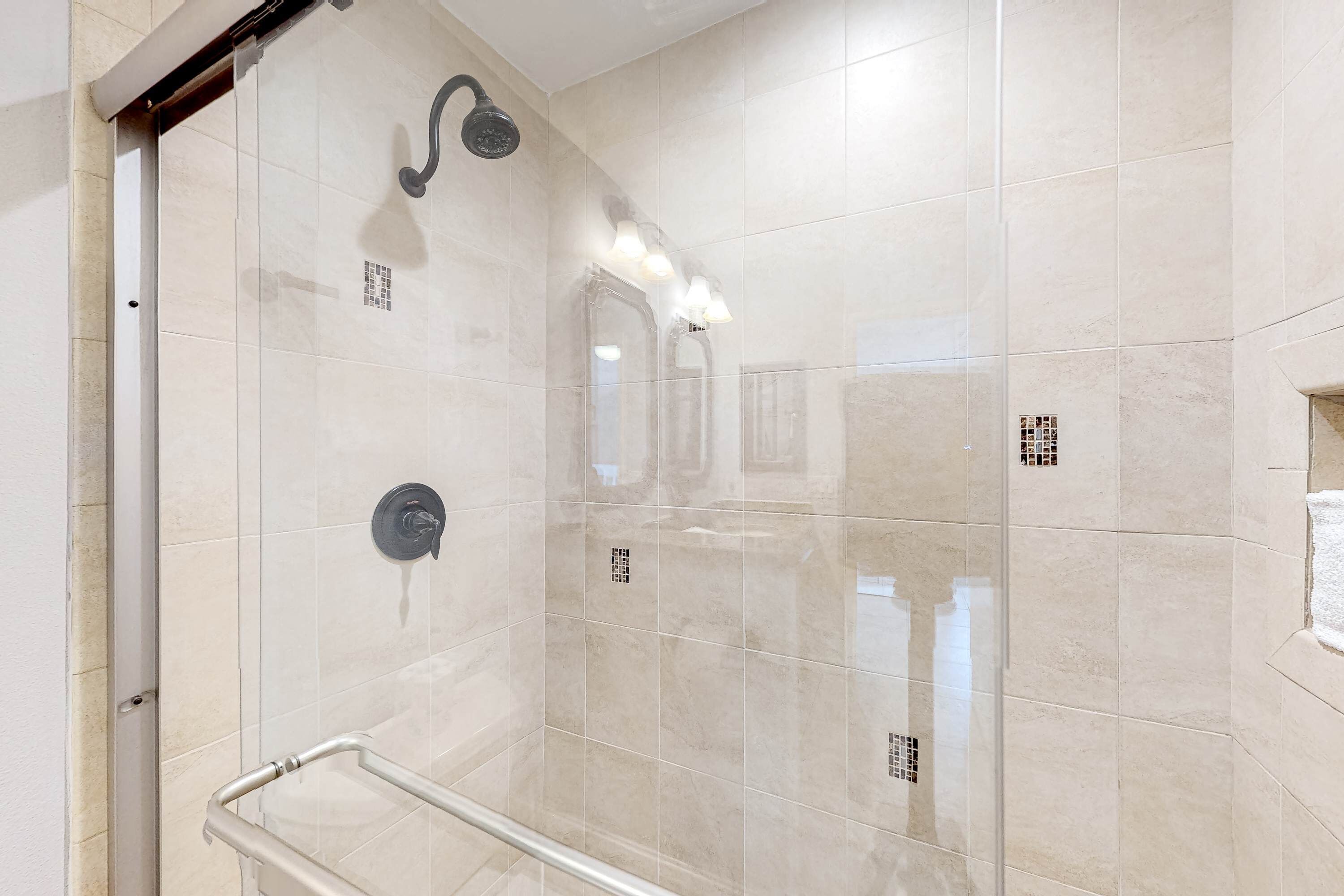 A modern bathroom with a glass shower enclosure, a handrail, and a wall-mounted showerhead.