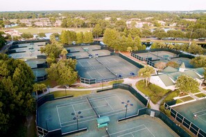 Ein Luftbild eines Sportkomplexes mit mehreren Tennisplätzen, umgeben von Bäumen und Wohngebäuden.