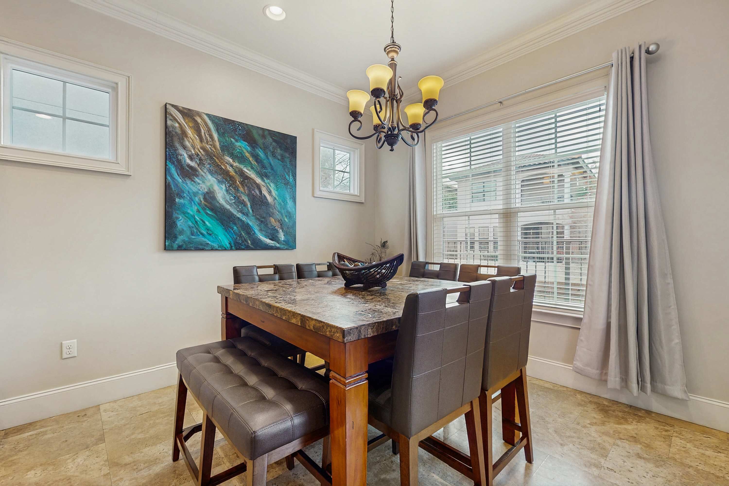 A dining area with a wooden table, chairs, a chandelier, and artwork on the wall.