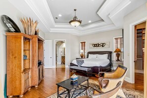 A spacious bedroom with a large bed, a wooden cabinet, a chair, and a small table. - Spacious Beach Home with Pool & Balconies - Short Walk to Private Beach Access (Miramar Beach)