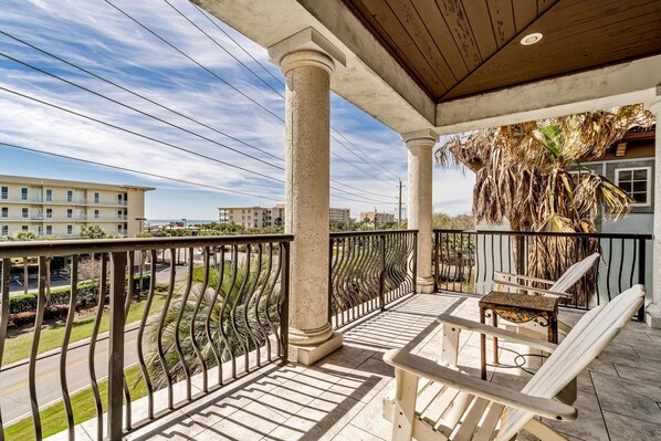 A balcony with white chairs and a table, overlooking a street and buildings. - Spacious Beach Home with Pool & Balconies - Short Walk to Private Beach Access (Miramar Beach)
