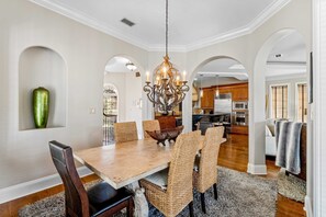 A dining room with a wooden table, wicker chairs, and a chandelier. There are arched doorways leading to other rooms. - Spacious Beach Home with Pool & Balconies - Short Walk to Private Beach Access (Miramar Beach)