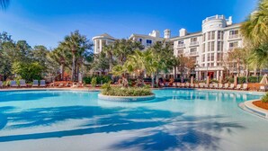 Ein großer Pool mit einer kreisförmigen Insel, umgeben von Palmen und Liegestühlen, mit einem großen Gebäude im Hintergrund.