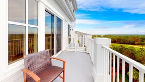 Ein Balkon mit einem Holzstuhl, weißen Geländern und Blick auf einen Golfplatz und Bäume.