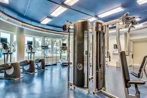 Un gimnàs amb diverses màquines d'exercici, incloent cintes de córrer i aparells de musculació, i grans finestres que ofereixen llum natural.