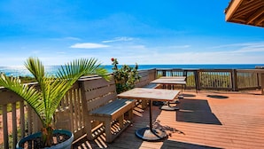 Une terrasse en bois avec des sièges d’extérieur, un palmier et une vue sur l’océan.