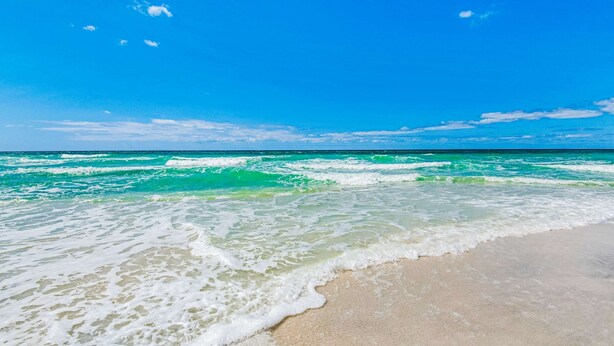 Une plage à l’eau turquoise et limpide, bordée d’un rivage sablonneux, sous un ciel d’un bleu éclatant.