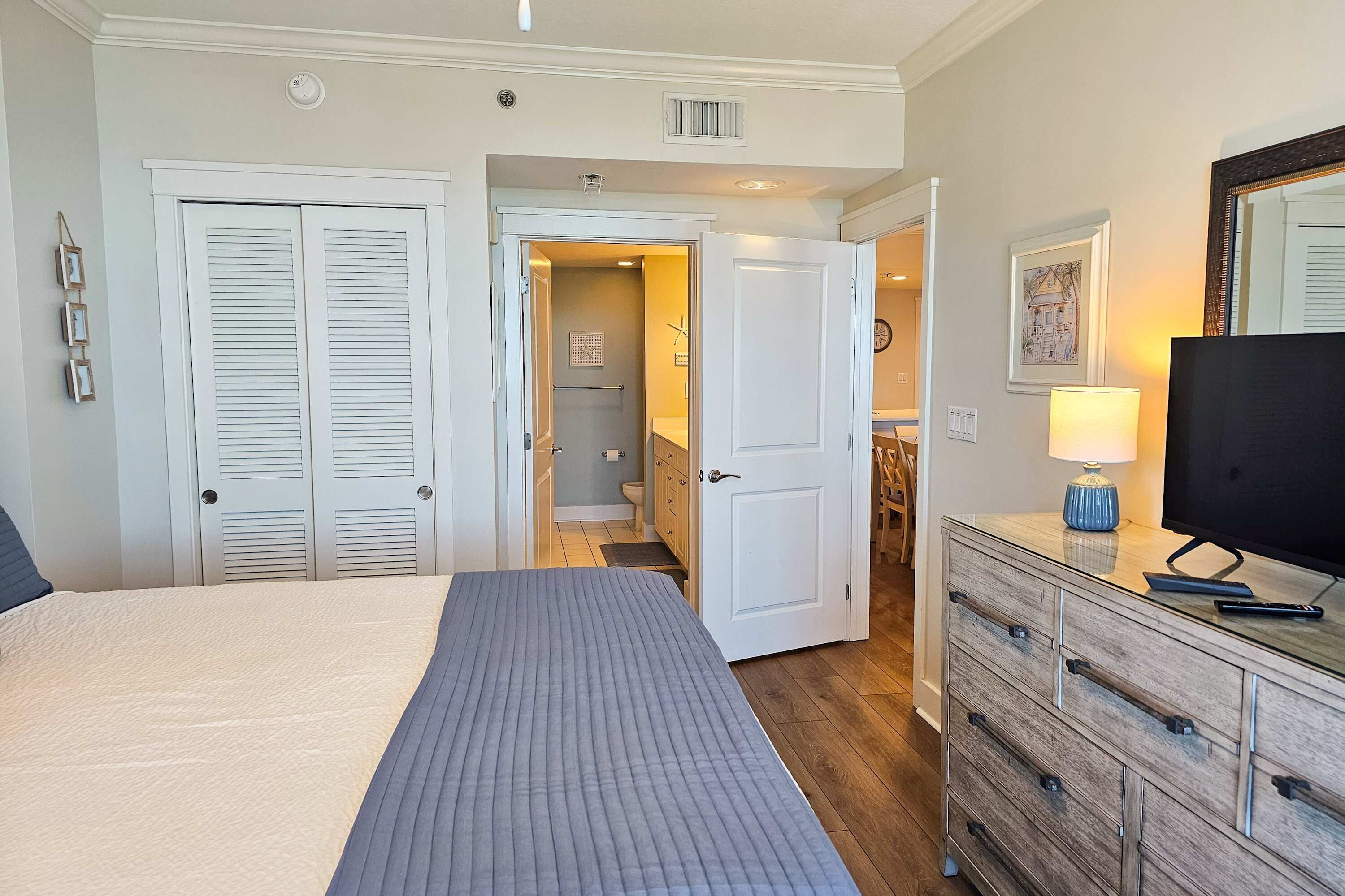 A hotel room with a bed, a dresser, a television, and a bathroom visible through an open door.