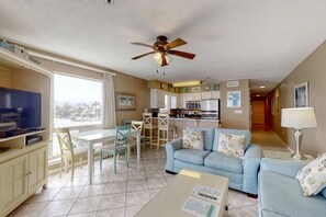 Ein Wohnzimmer mit Fernseher, Essbereich, einer Küchenzeile und einem Deckenventilator.
