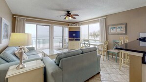 Camera d'albergo con divano, un piccolo tavolo, televisione, ventilatore a soffitto e un balcone con vista.
