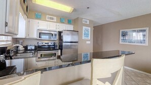 Una cucina con mobili bianchi, elettrodomestici in acciaio inossidabile, un piano di lavoro in granito e una sedia.