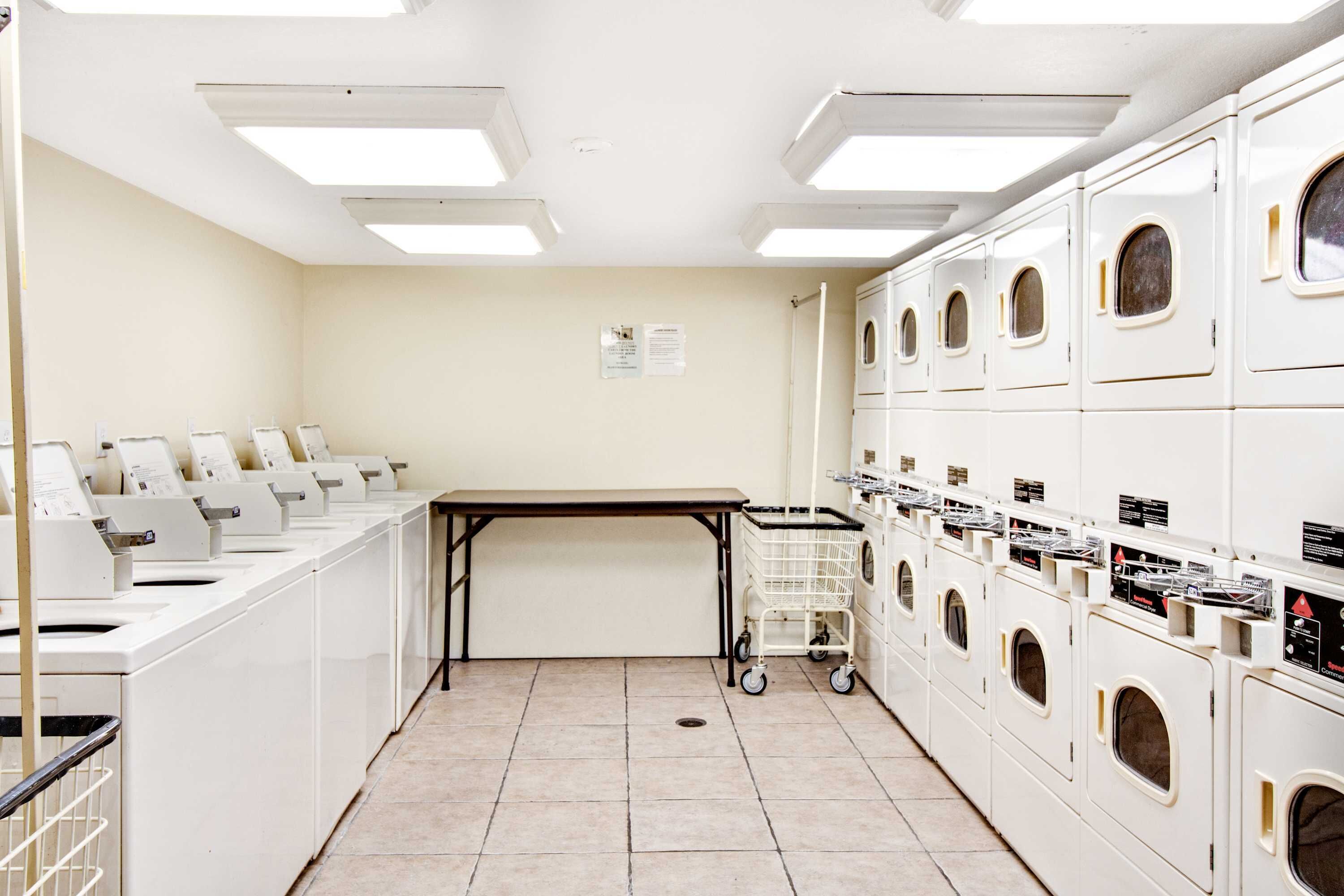 A laundry facility with multiple washing machines and dryers, a table, and a cart.