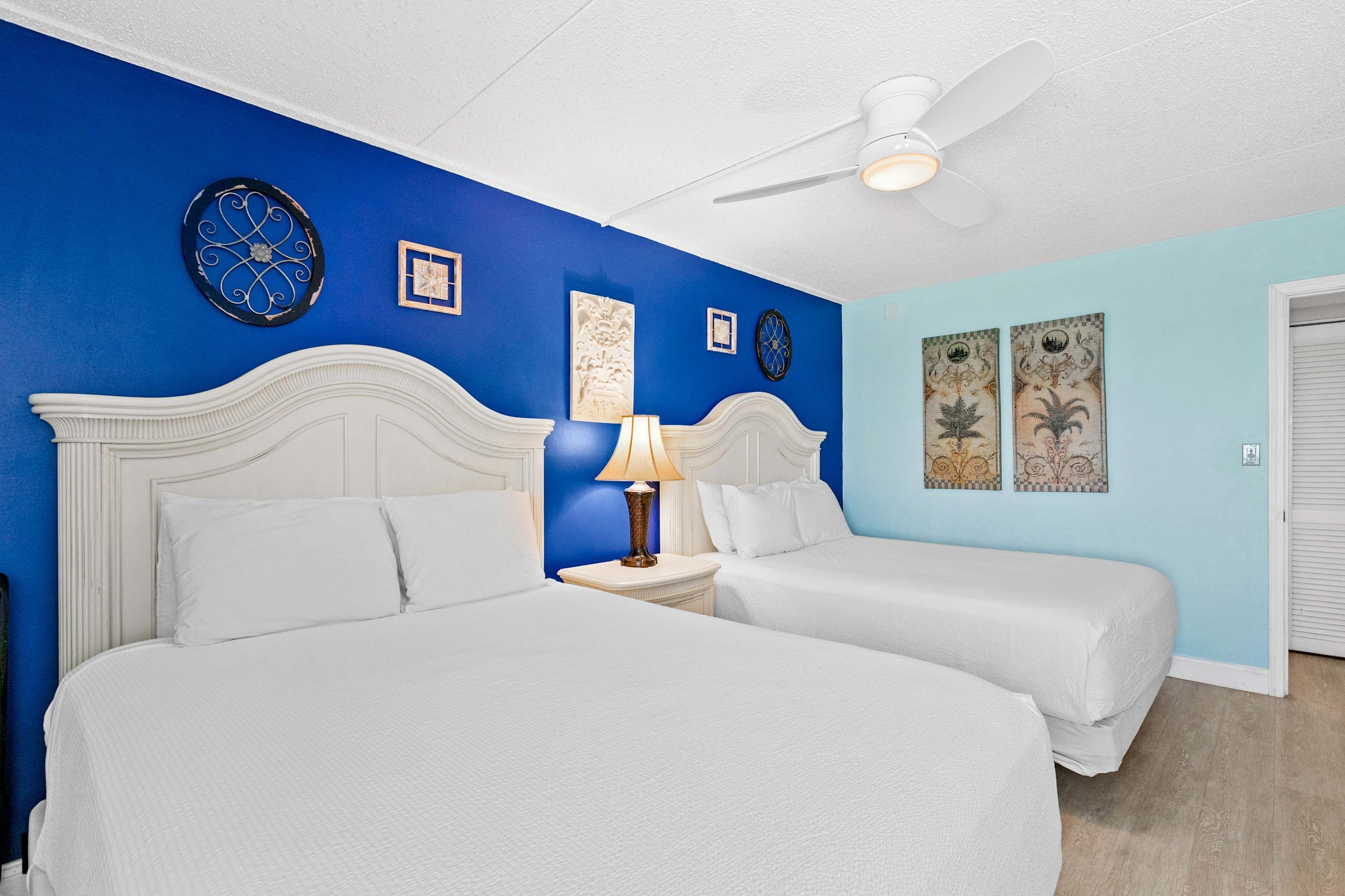 A hotel room with two beds, a ceiling fan, and decorative wall art.
