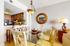Une cuisine moderne avec des meubles en bois, un coin repas avec une table et des chaises en verre, un lustre, un miroir rond et une lampe.