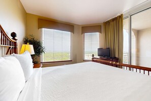 Une chambre d’hôtel avec un grand lit, un téléviseur posé sur un meuble en bois et un balcon avec des rideaux.
