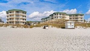 Un hotel frente a la playa con varios balcones, una estación de salvavidas y una playa arenosa al frente.