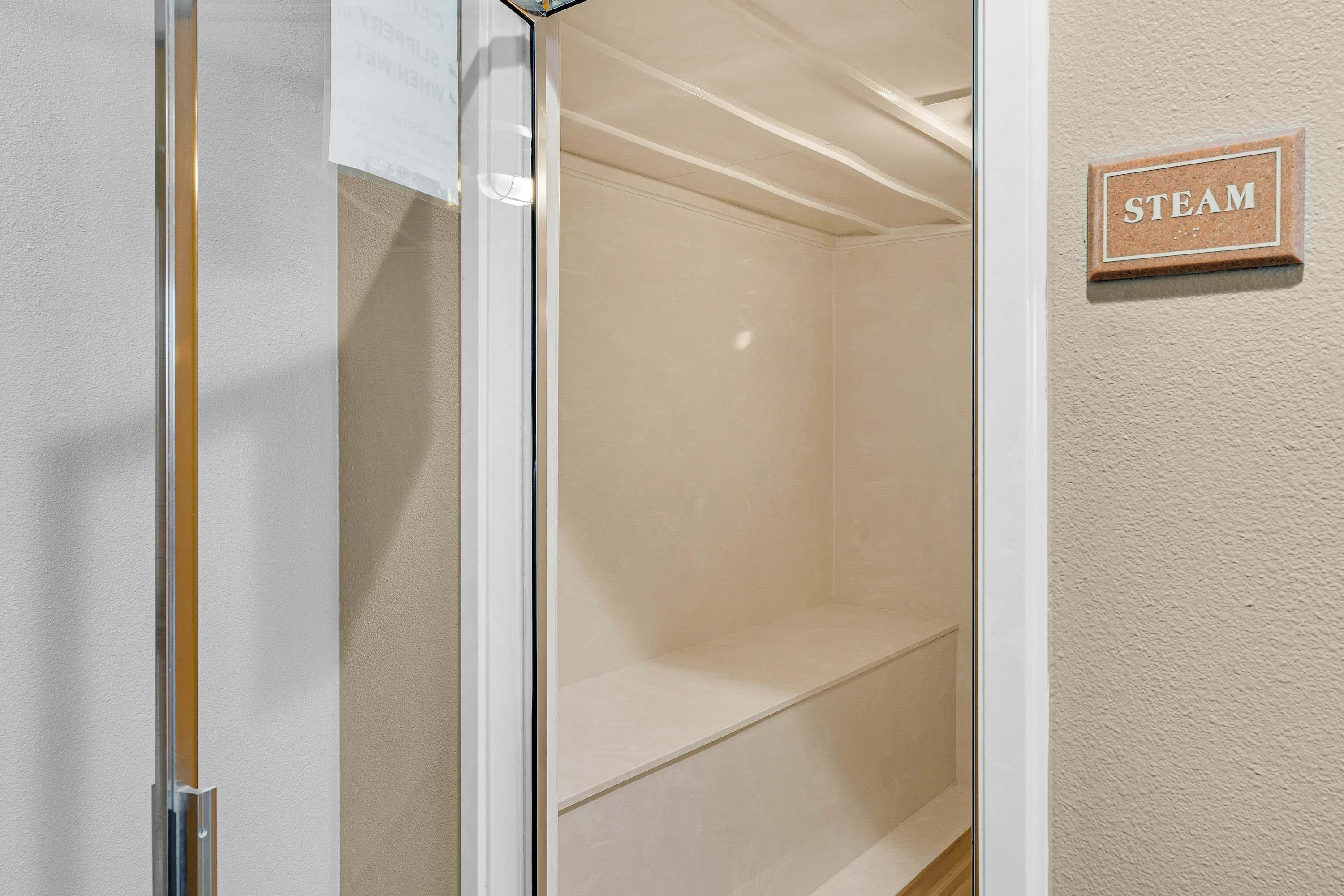A room with a glass door leading to a shower area, a sign labeled "STEAM", and a plain wall.