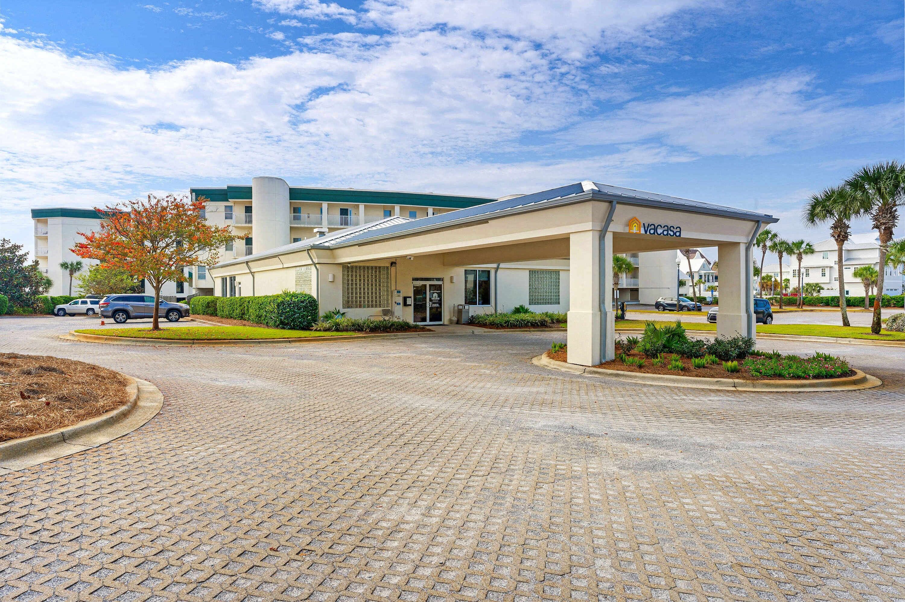 A hotel entrance with a covered parking area, a sign for 'Vacasa', and a building with a green roof and multiple balconies.