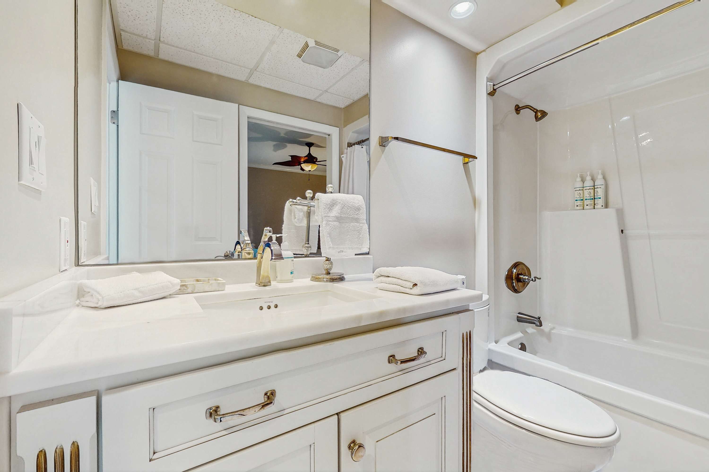 Un bagno con un mobile lavabo bianco, un water, una doccia con porta in vetro e una ventola a soffitto.