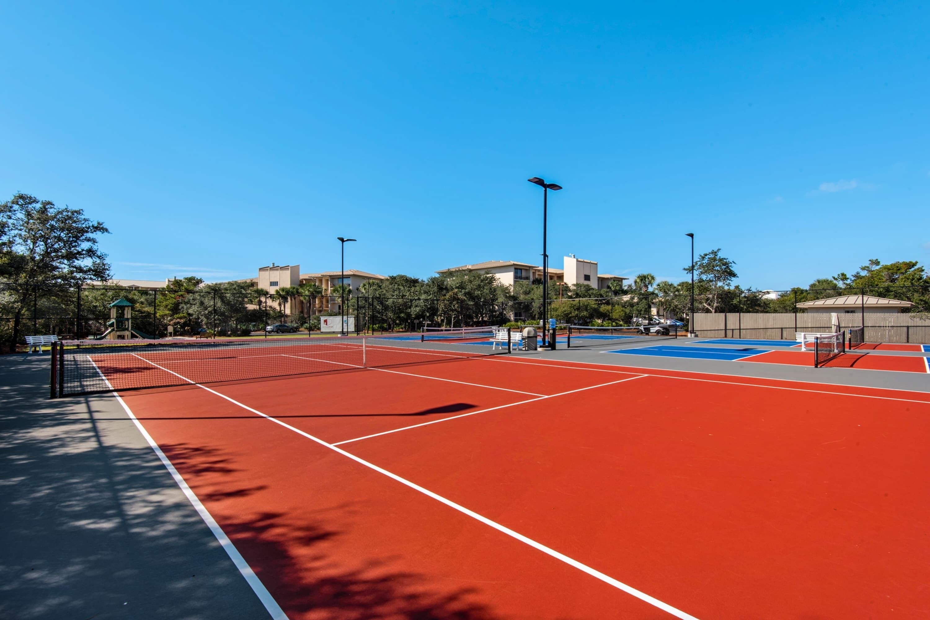 A tennis court with a net, surrounded by trees and buildings.