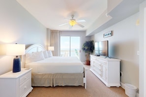 A bedroom with a bed, nightstand, dresser, TV, and a ceiling fan. - Gorgeous beachfront condo, shared pool and beach access (Panama City Beach)