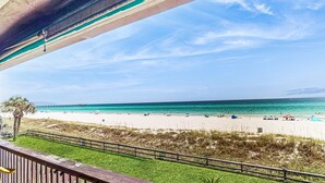 Vista sulla spiaggia da un balcone con ringhiera in legno, cielo sereno e spiaggia sabbiosa con persone e ombrelloni.