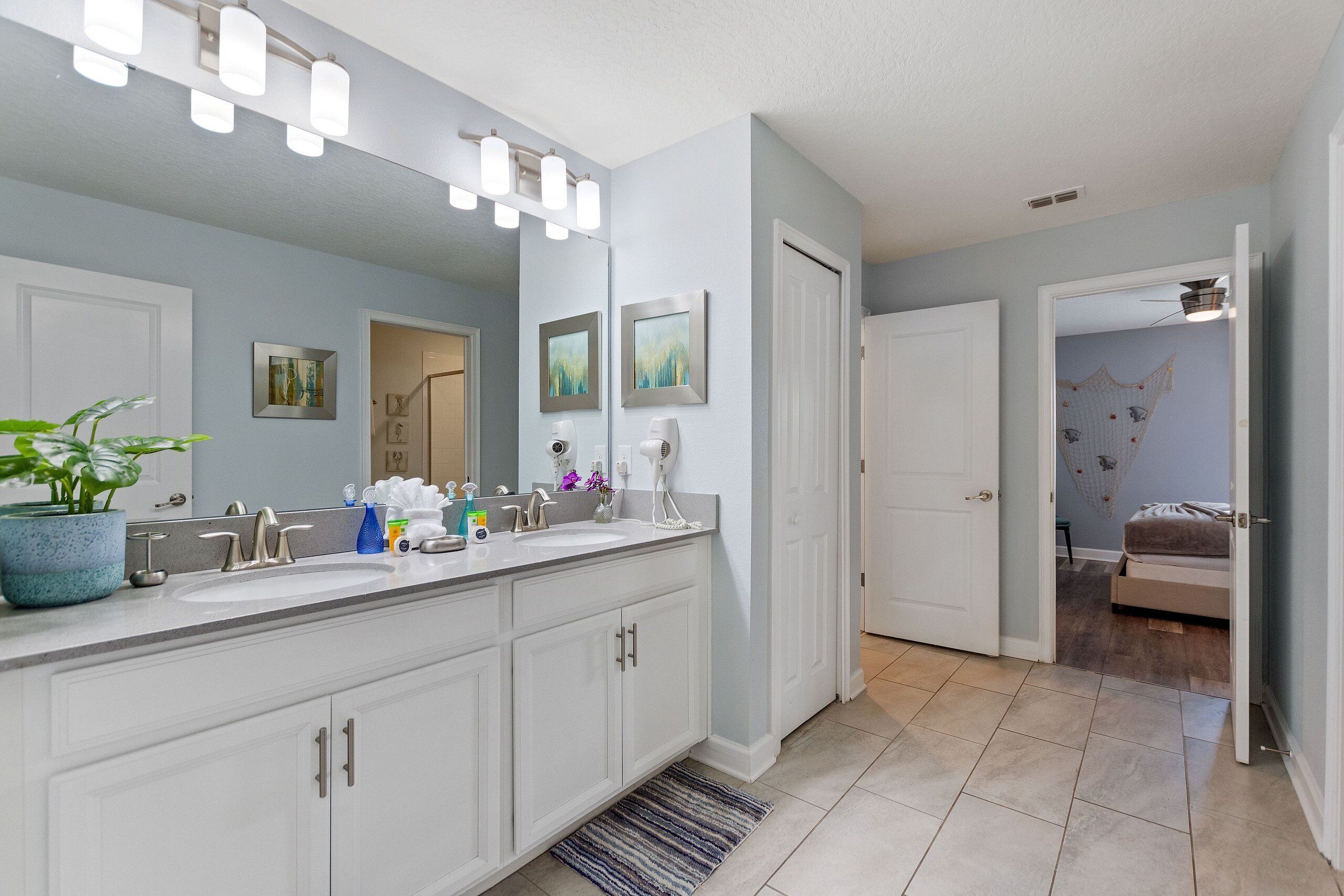 A modern bathroom with a large mirror, two sinks, and a potted plant.