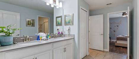 A modern bathroom with a large mirror, two sinks, and a potted plant.