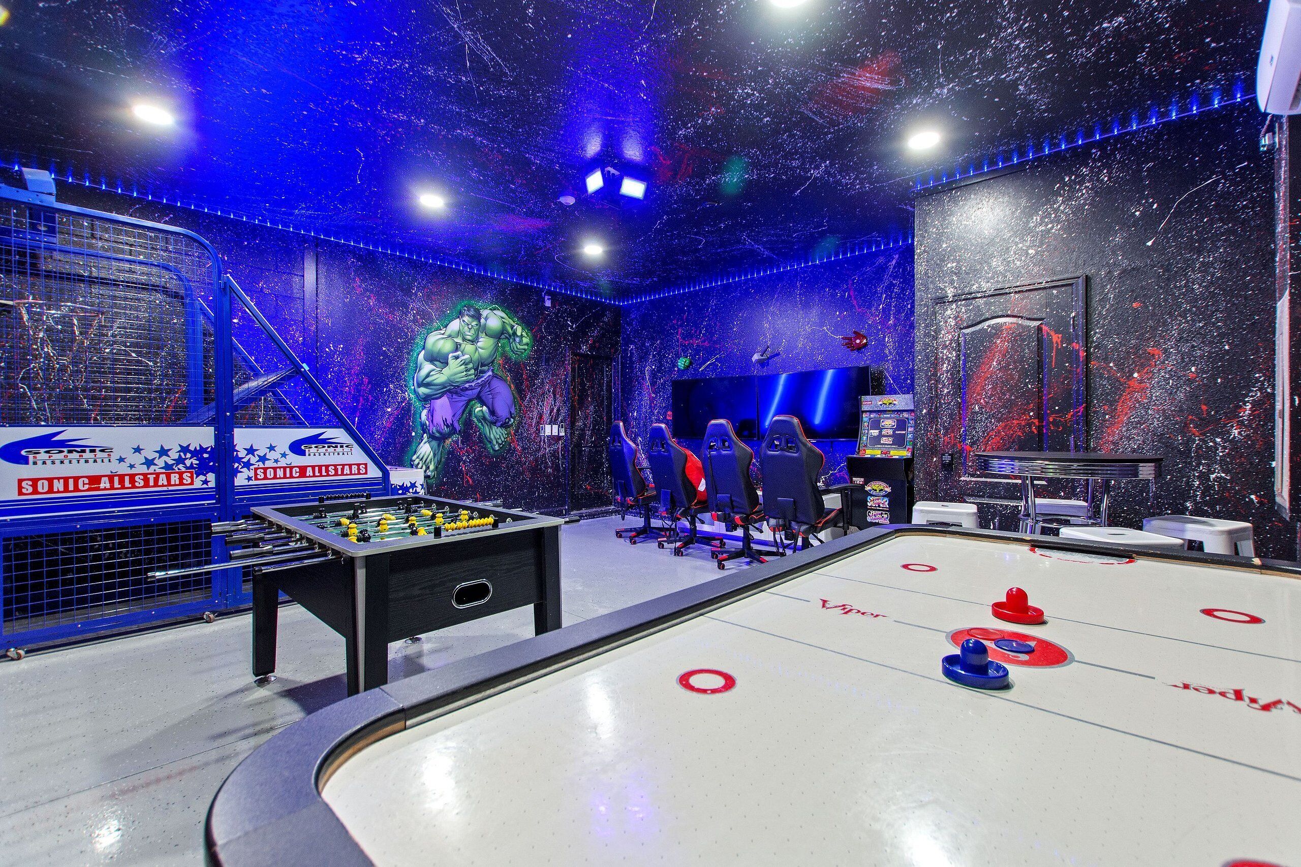 An indoor recreational area with a foosball table, shuffleboard table, and arcade machines.