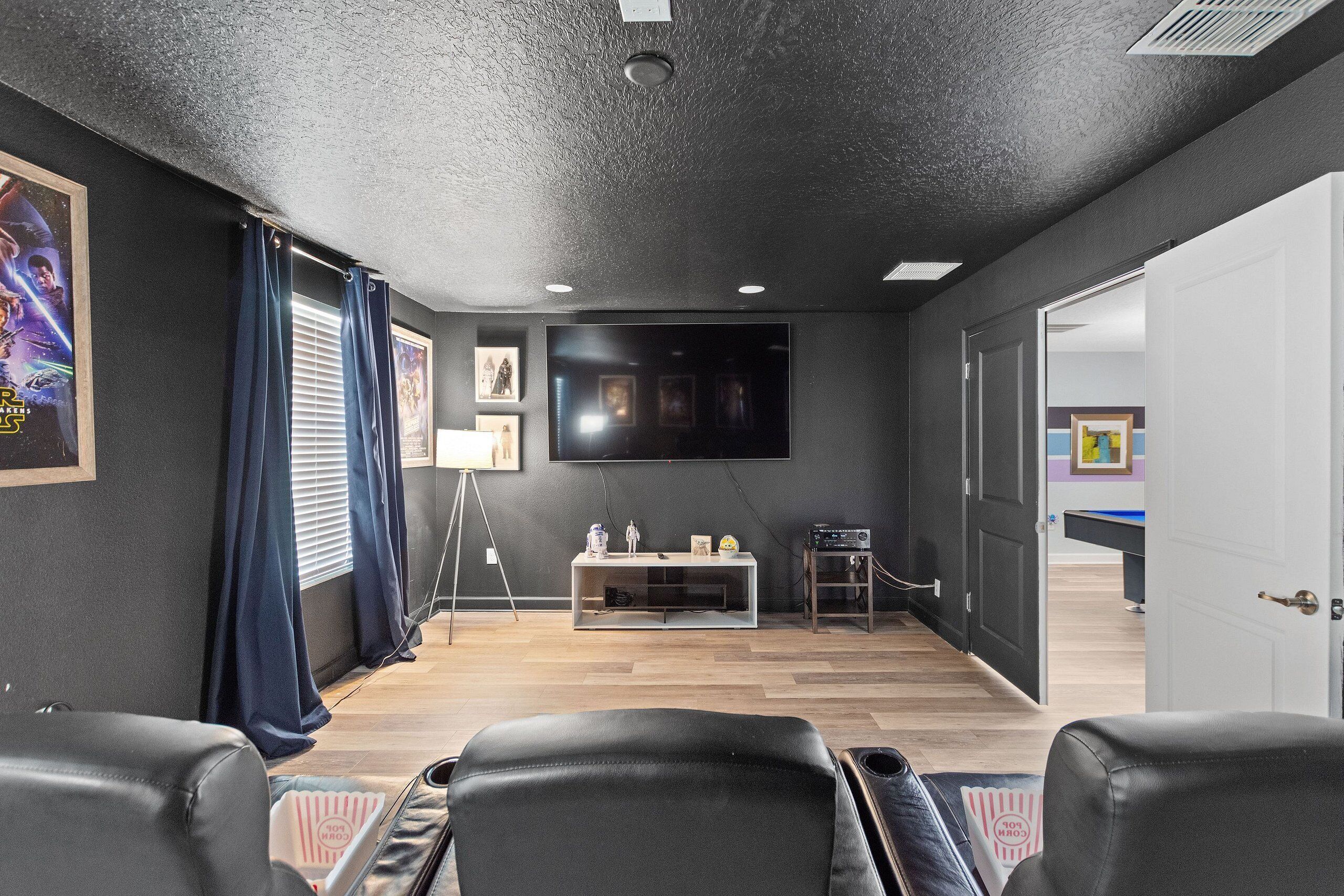 A home theater room with a large flat-screen TV, a gaming console, and a pool table.