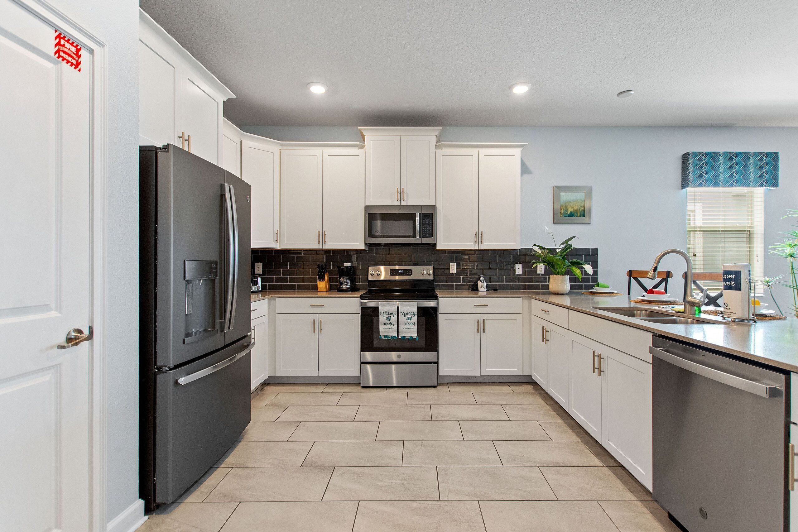 A modern kitchen with white cabinets, stainless steel appliances, and a tiled backsplash.