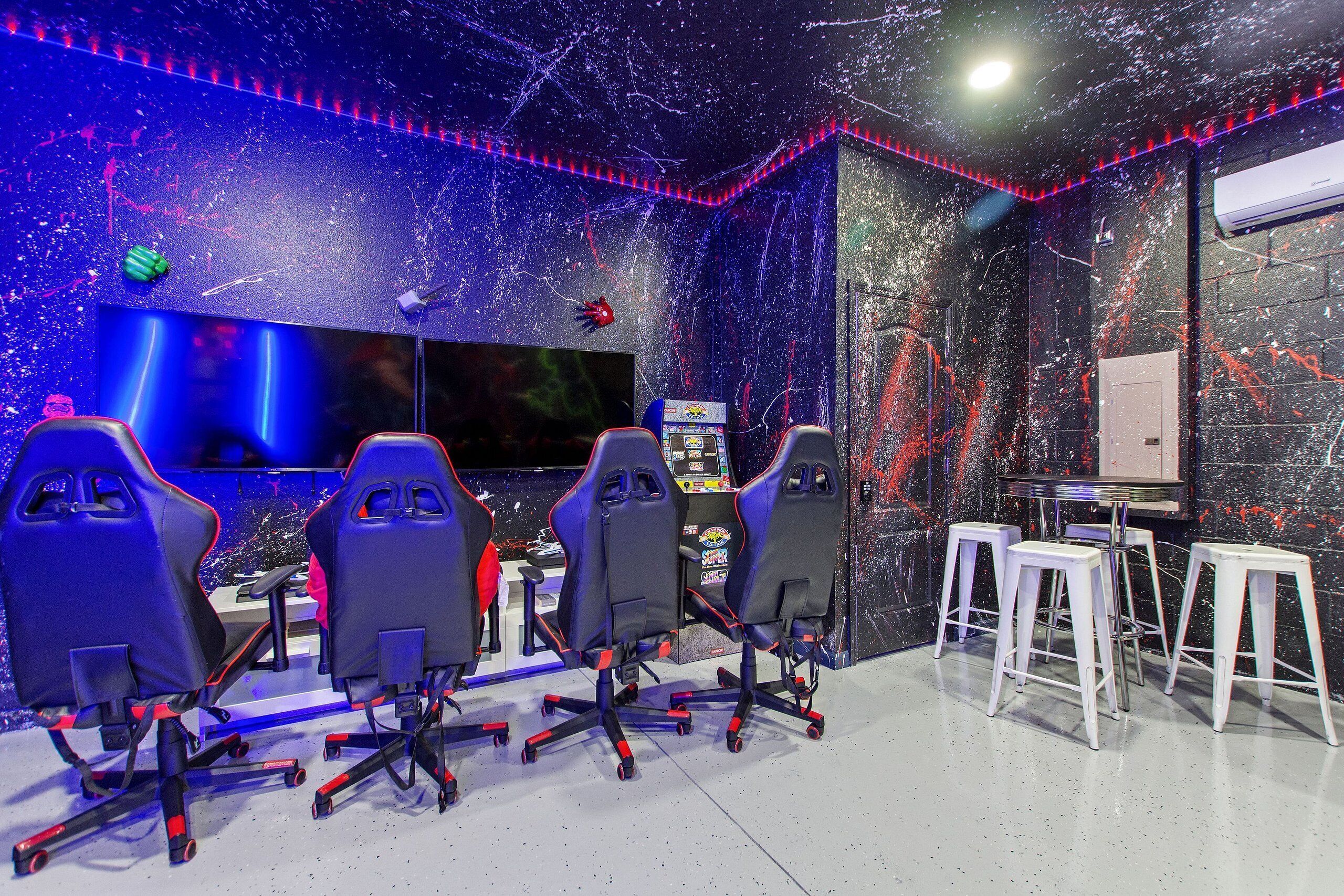 Una sala de jocs amb quatre seients gamer, un monitor gran i un panell de control.