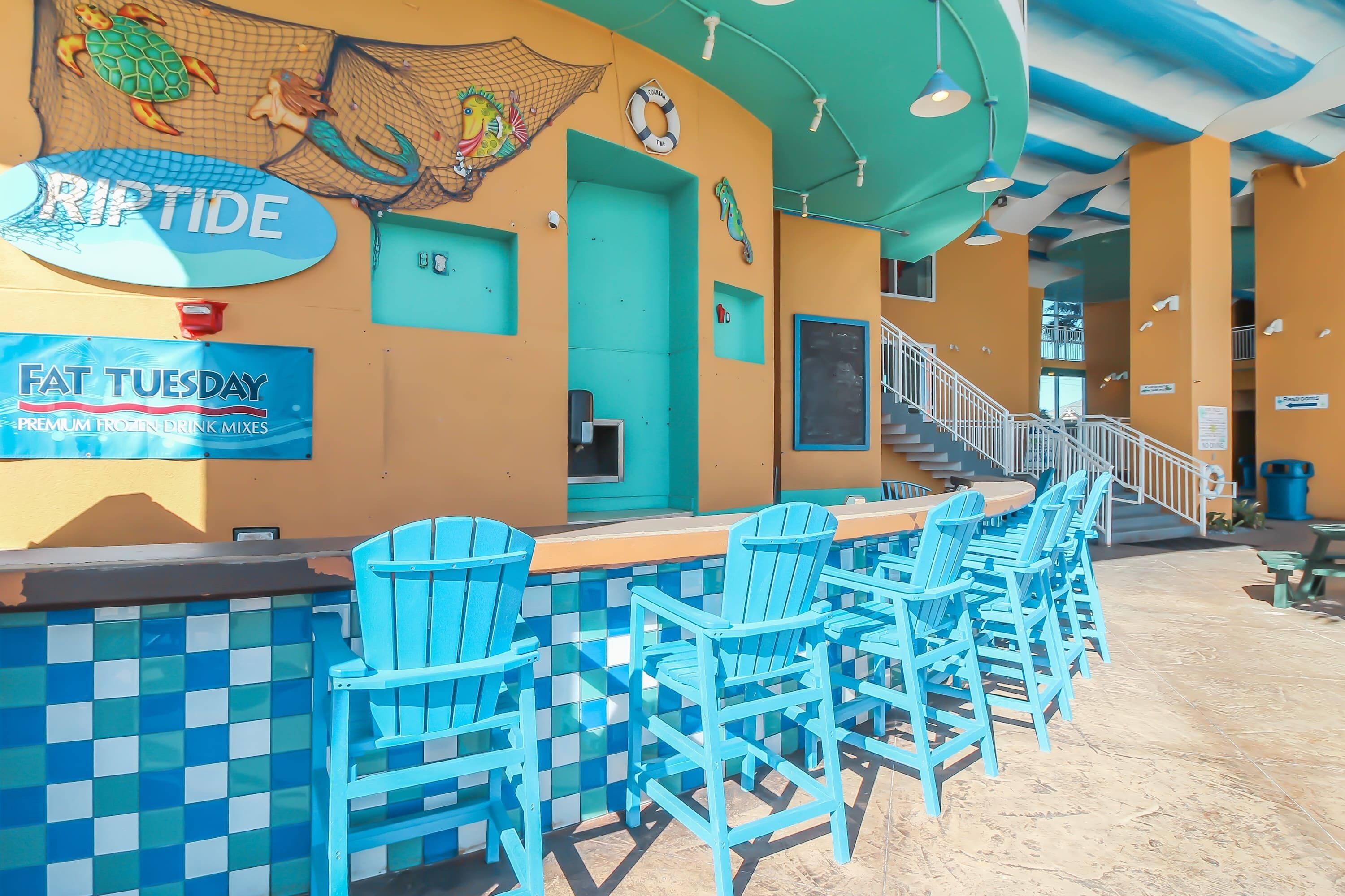 Zona de bar con una puerta turquesa, un letrero que dice 'RIPTIDE' y un letrero que anuncia 'FAT TUESDAY' con mezclas heladas de primera calidad.