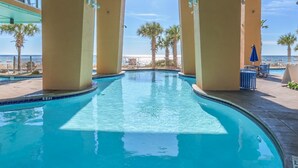 A swimming pool with a view of the beach, palm trees, and a clear sky. - 16th-floor oceanfront condo with ocean view, WiFi, and hot tub/pool (Panama City Beach)