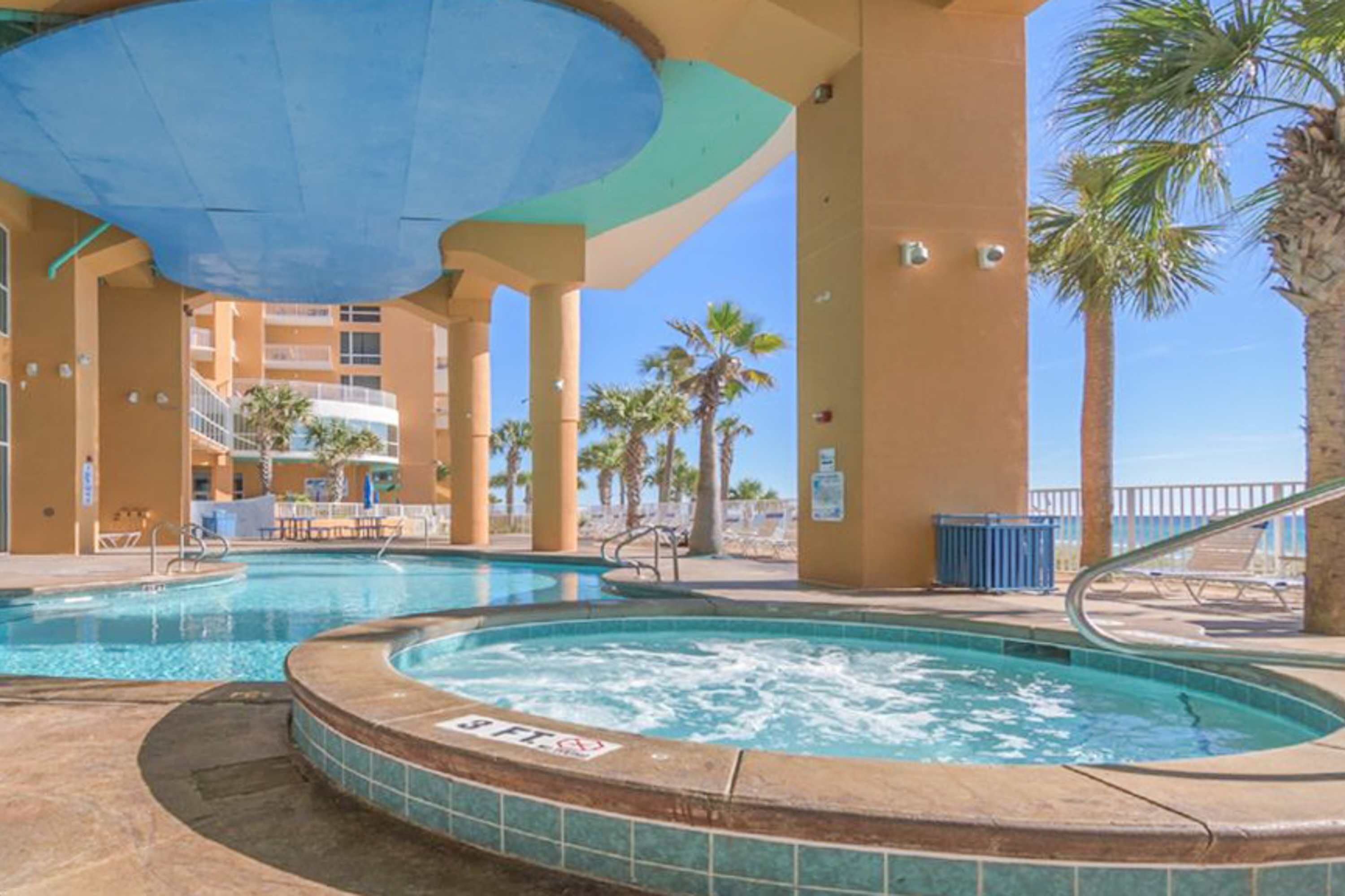 A pool area with a hot tub, palm trees, and a covered seating area.