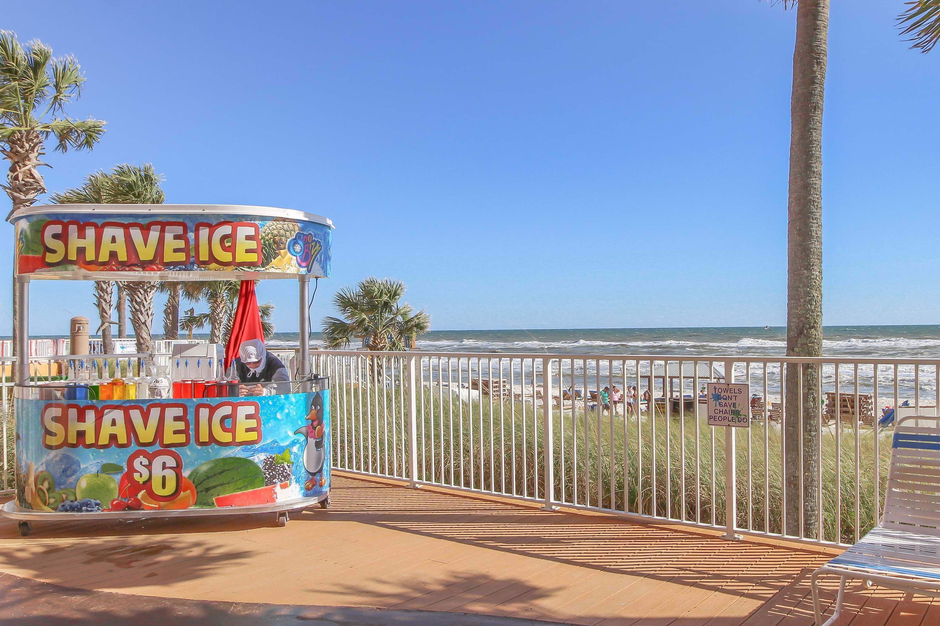 Un chariot à crème glacée installé sur la plage, avec une pancarte indiquant « GRANITÉS 6 $ » et un panneau d’avertissement concernant les serviettes.