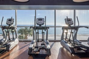 Ein Fitnessraum mit Cardiogeräten und Blick auf den Strand.