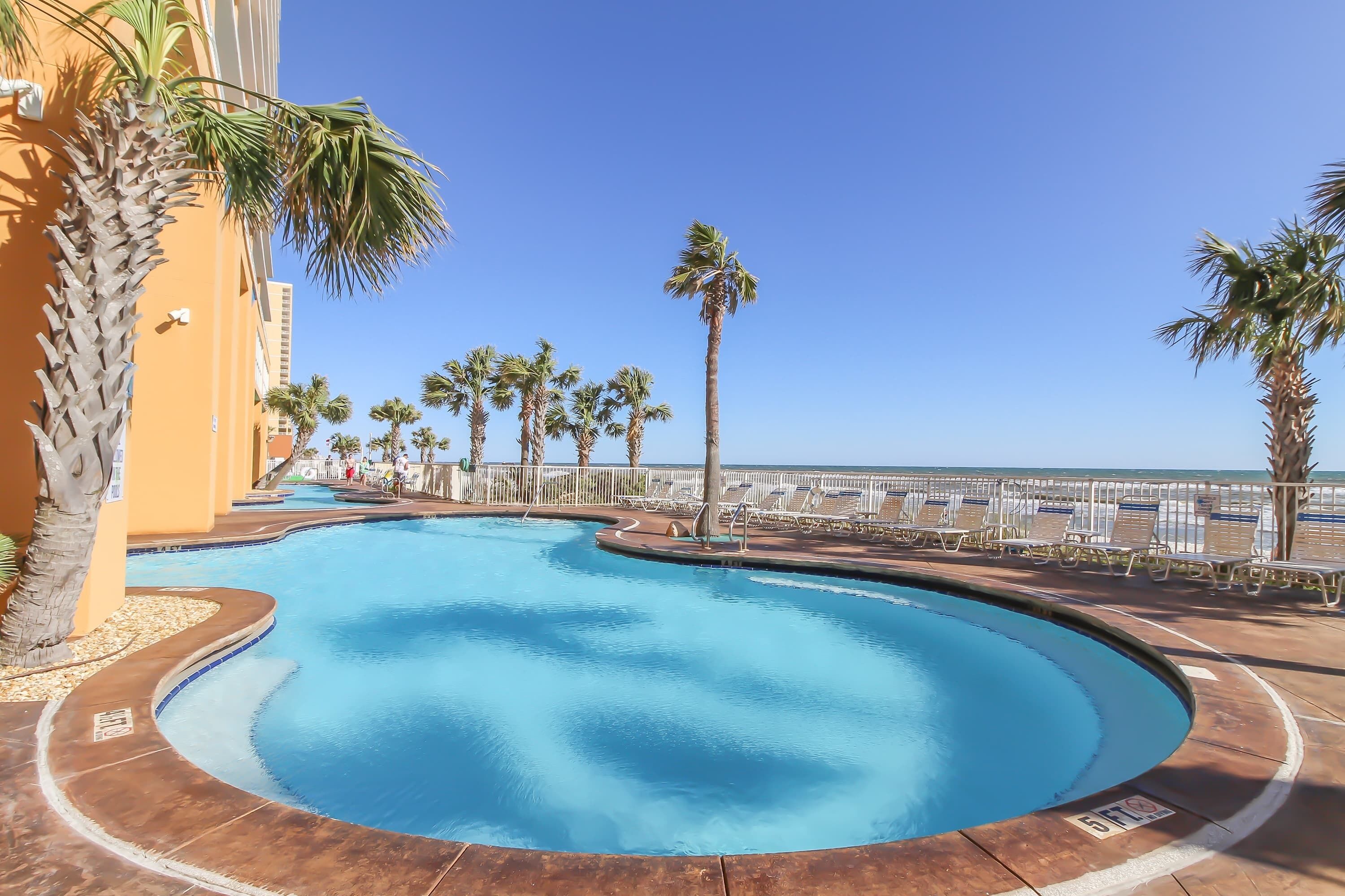A swimming pool with palm trees, a poolside area, and a view of the ocean.