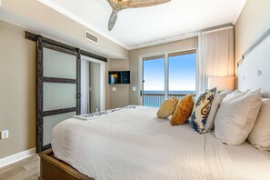Ein Schlafzimmer mit einem großen Bett, einer Schiebetür, einem an der Wand befestigten Fernseher und Blick auf den Ozean.