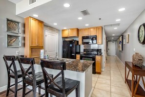 Una cocina con armarios de madera, encimera de granito y zona de comedor con sillas de madera oscura.