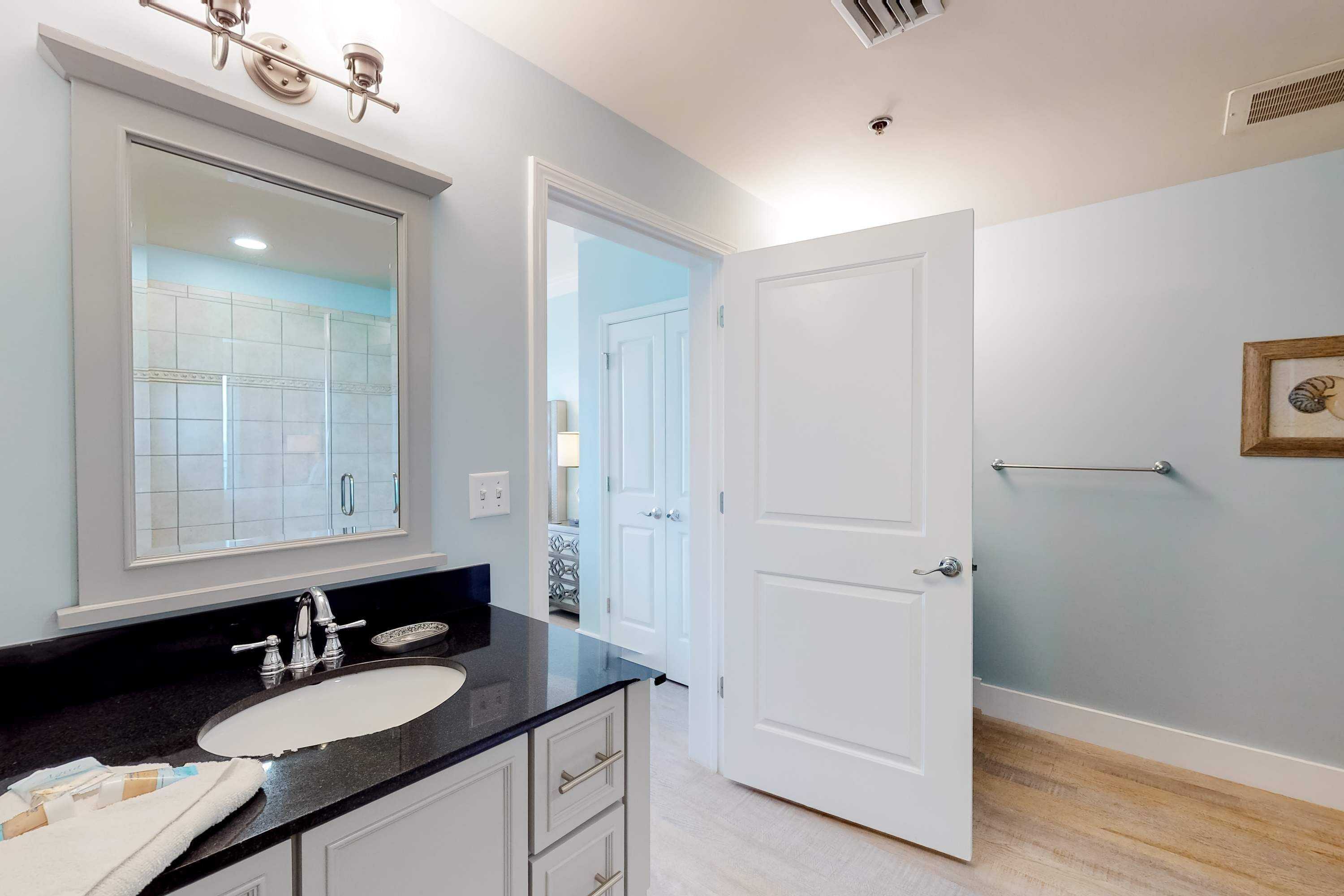Un baño con un espejo grande, un lavamanos y una puerta que da a otra habitación.