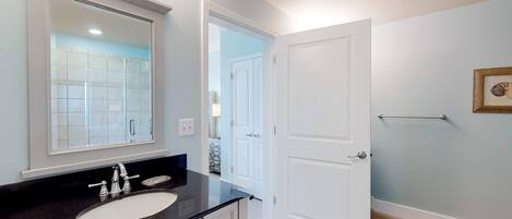 Un baño con un espejo grande, un lavamanos y una puerta que da a otra habitación.