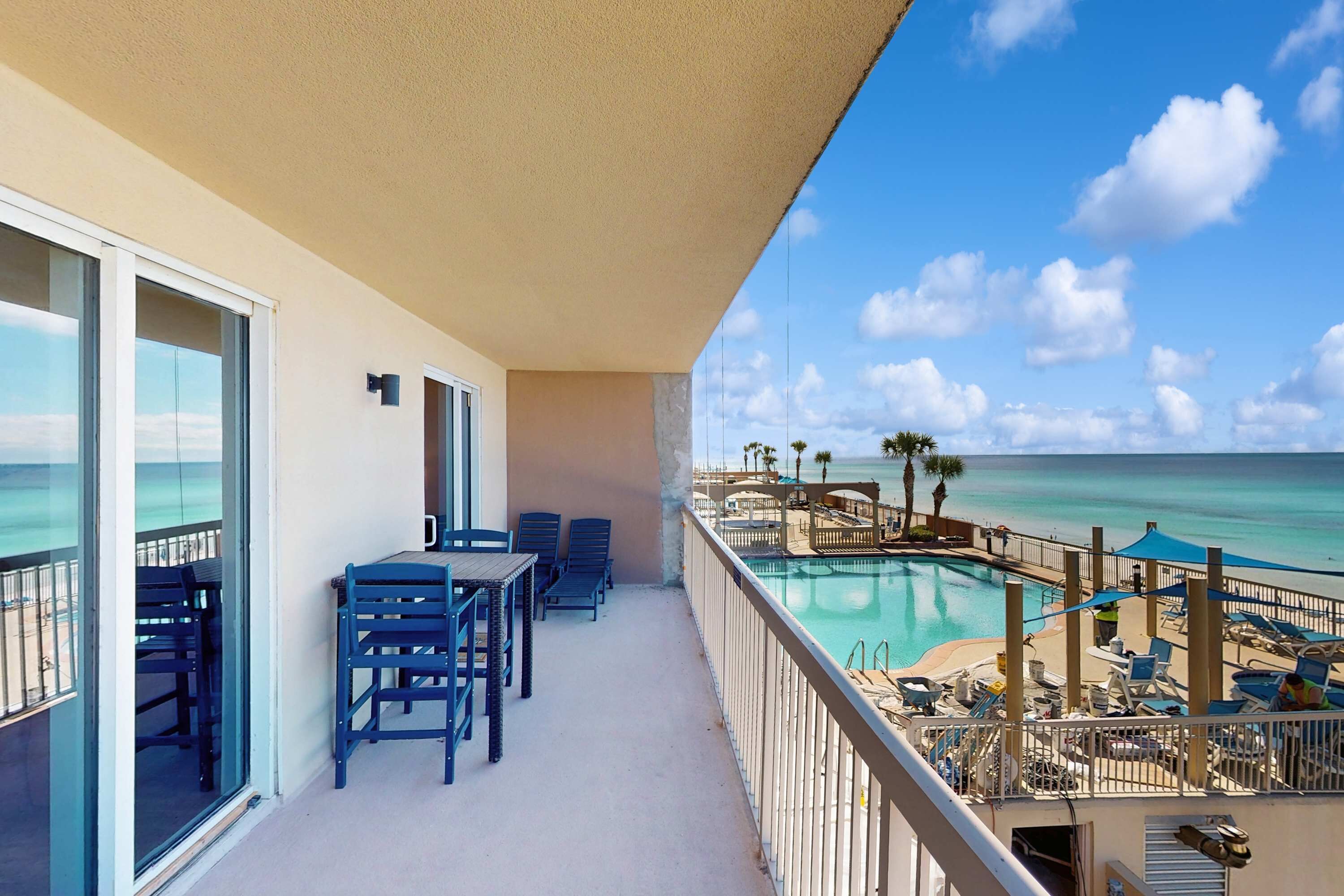 A balcony with a pool view, outdoor seating, and a clear sky.